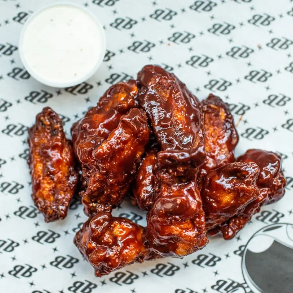 Bozzelli's BBQ chicken wings with a side of ranch dressing on branded parchment paper.
