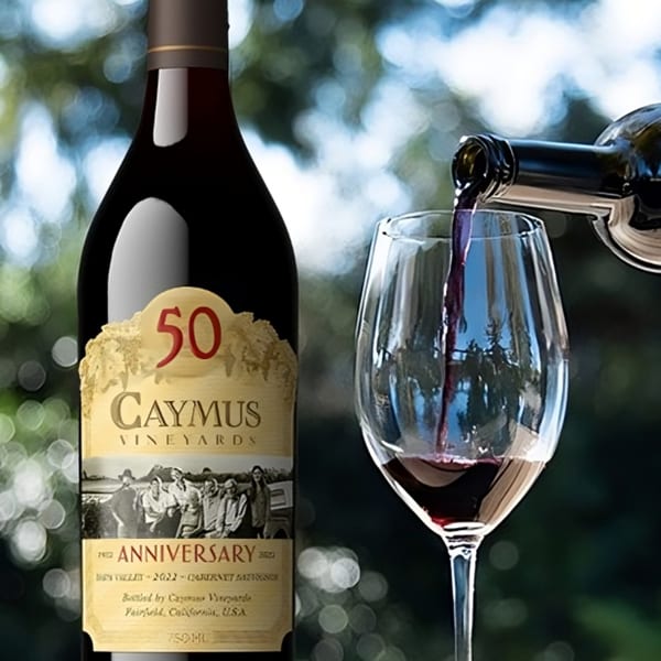 A bottle of Caymus Vineyards 50th Anniversary wine next to a glass being filled with red wine.