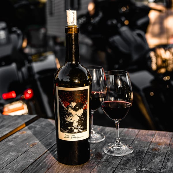 A bottle of "The Prisoner" red wine and two glasses with red wine on a wooden table.