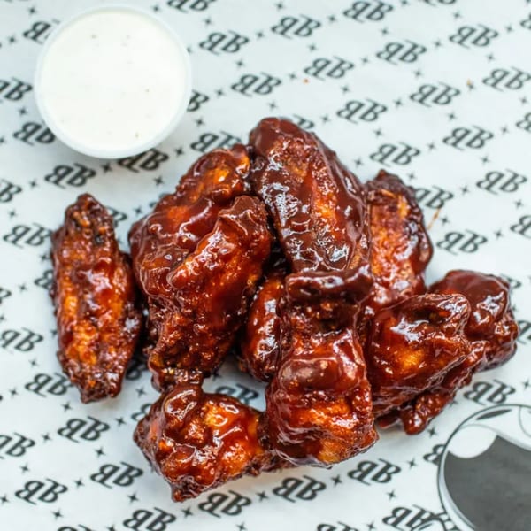 Bozzelli's BBQ chicken wings with a side of ranch dressing on branded parchment paper.