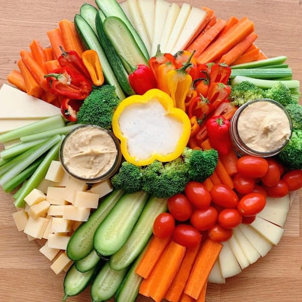 A colorful Bozzelli's veggie platter with carrots, celery, cucumbers, bell peppers, broccoli, tomatoes, cheese, and hummus.
