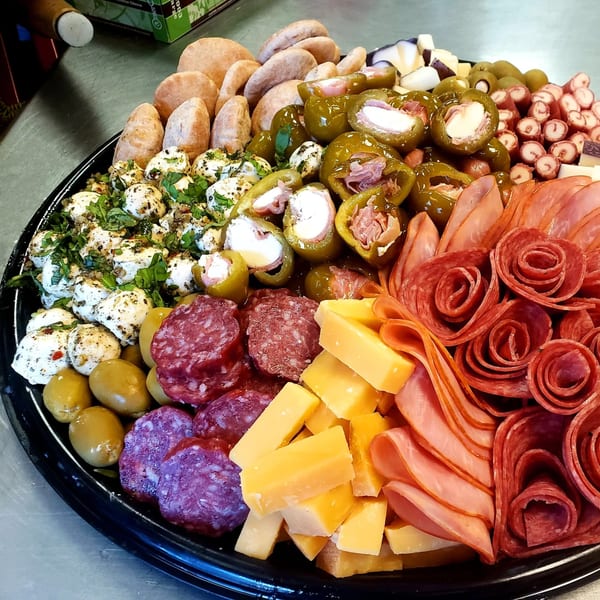 A large Bozzelli's catering platter with various meats, cheeses, olives, stuffed peppers, and bread.