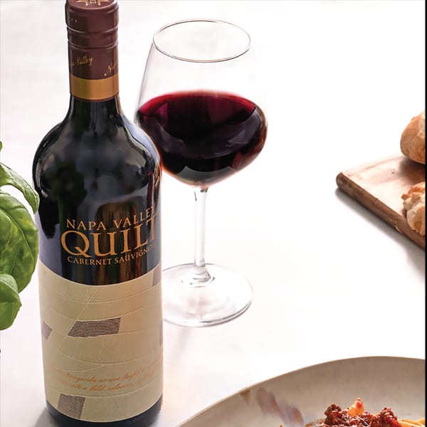 A bottle of Napa Valley Quilt Cabernet Sauvignon, a glass of red wine, and pasta.