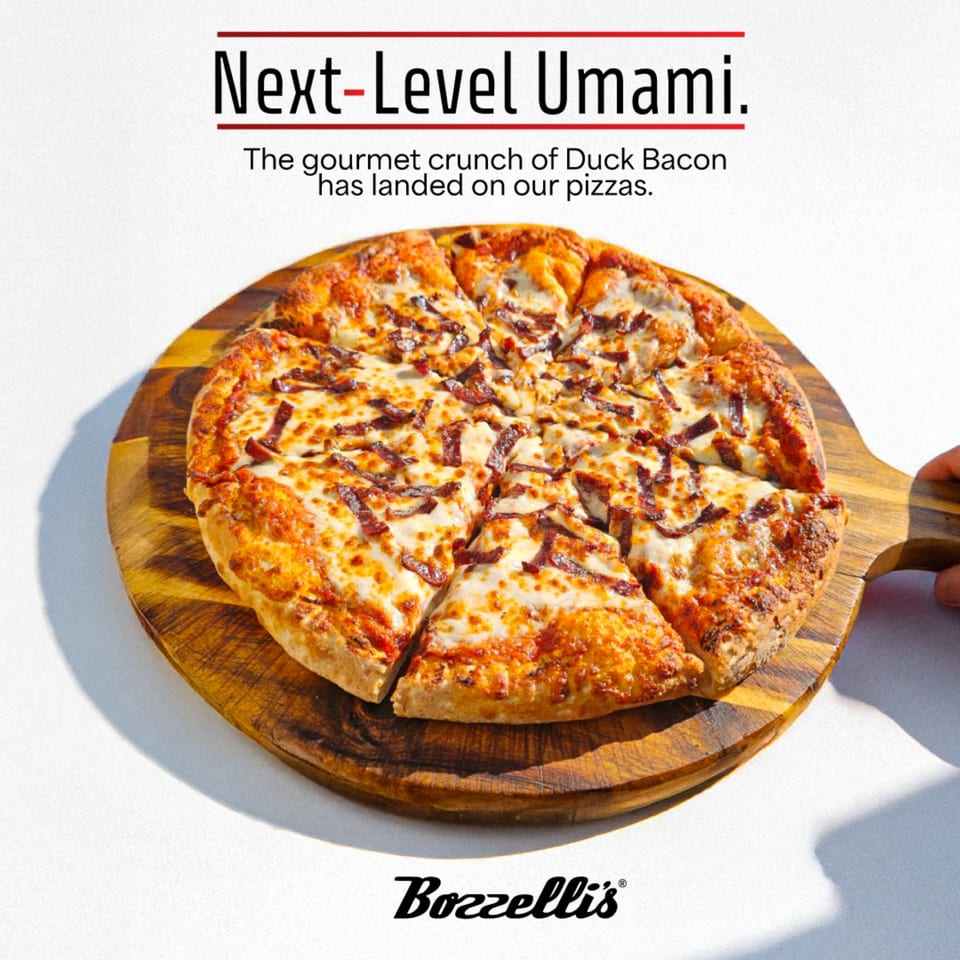 Bozzelli's duck bacon pizza, sliced and served on a wooden cutting board.
