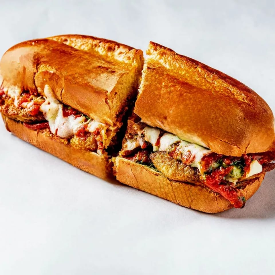 A Bozzelli's chicken parmesan sub, cut in half, with melted cheese and red sauce.