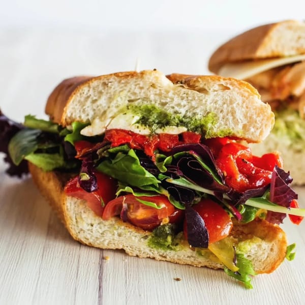 A Bozzelli's sub sandwich filled with fresh greens, tomatoes, roasted red peppers, and pesto.